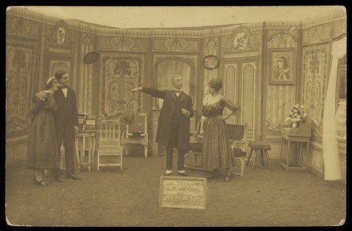 Download the full-sized image of Amateur actors, some in drag, posing on stage for "Miquette & sa mere"; at Sennelager prisoner of war camp in Germany. Photographic postcard, 191-.