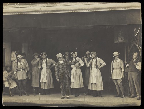 Download the full-sized image of Sailors, some in drag, stand on stage performing a scene. Photographic postcard, 191-.