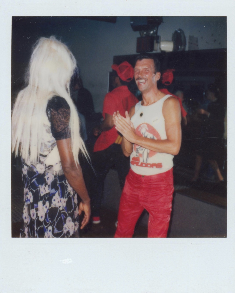 Download the full-sized image of A Photograph of Marsha P. Johnson with Long Blonde Hair and Wearing a Black and Pink Patterned Dress From Behind